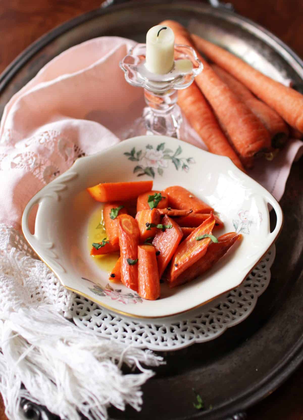 a plate of cooked carrots on a silver tray next to a few raw carrots.