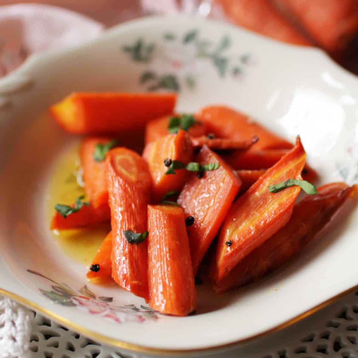 a close up picture of a bowl of cooked carrots next to a pink napkin