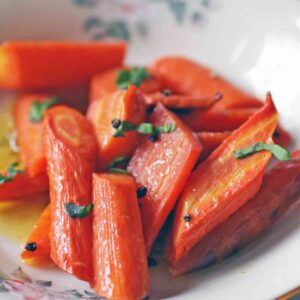 a white plate filled with roasted carrots topped with chopped parsley.