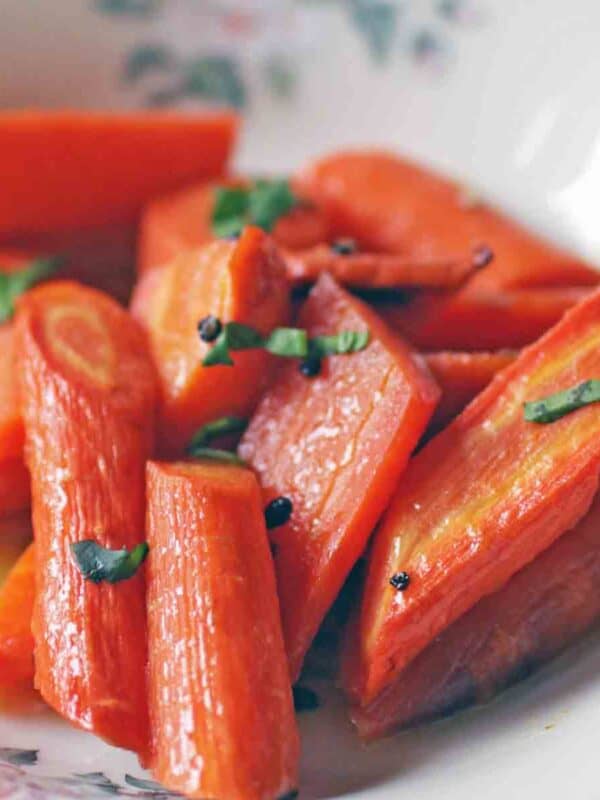 a white plate filled with roasted carrots topped with chopped parsley.