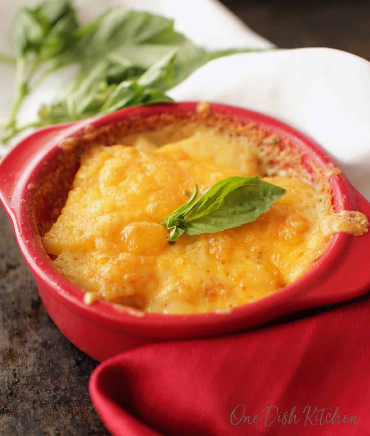a red bowl filled with cheese topped scalloped potatoes on a silver tray.