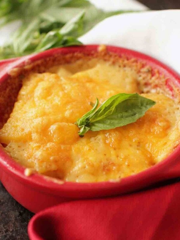 cheesy scalloped potatoes au gratin in a red baking dish next to fresh basil