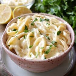 a pink bowl filled with fettuccine alfredo next to sliced lemons