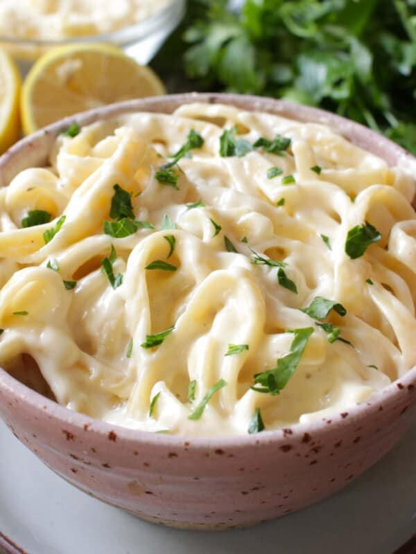 a pink bowl filled with fettuccine alfredo next to sliced lemons
