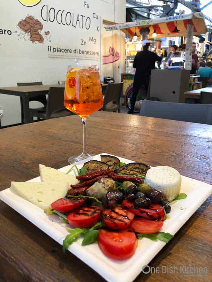 Enjoying and Aperol Spritz at an outdoor market with a plate of assorted appetizers