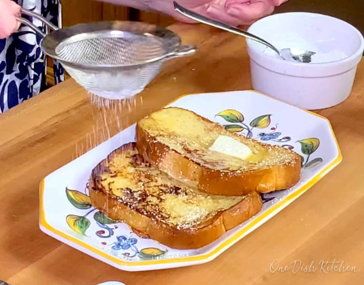 two slices of french toast on a white plate topped with powdered sugar.