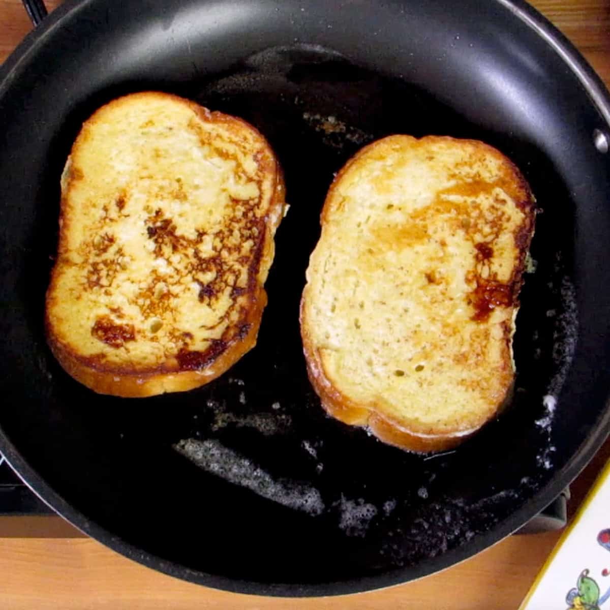 two slices of french toast cooking in a skillet.