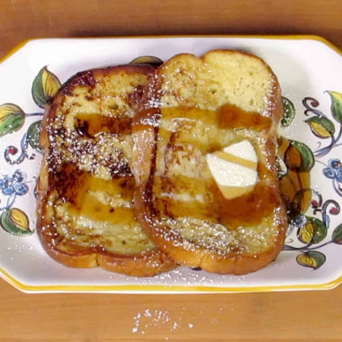 two slices of french toast on a plate topped with butter and syrup.