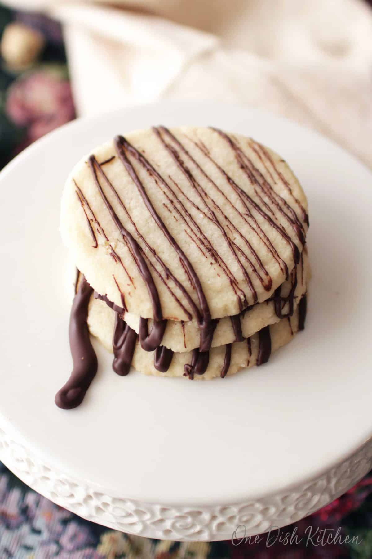 three cookies with a chocolate drizzle sitting on a cake stand.