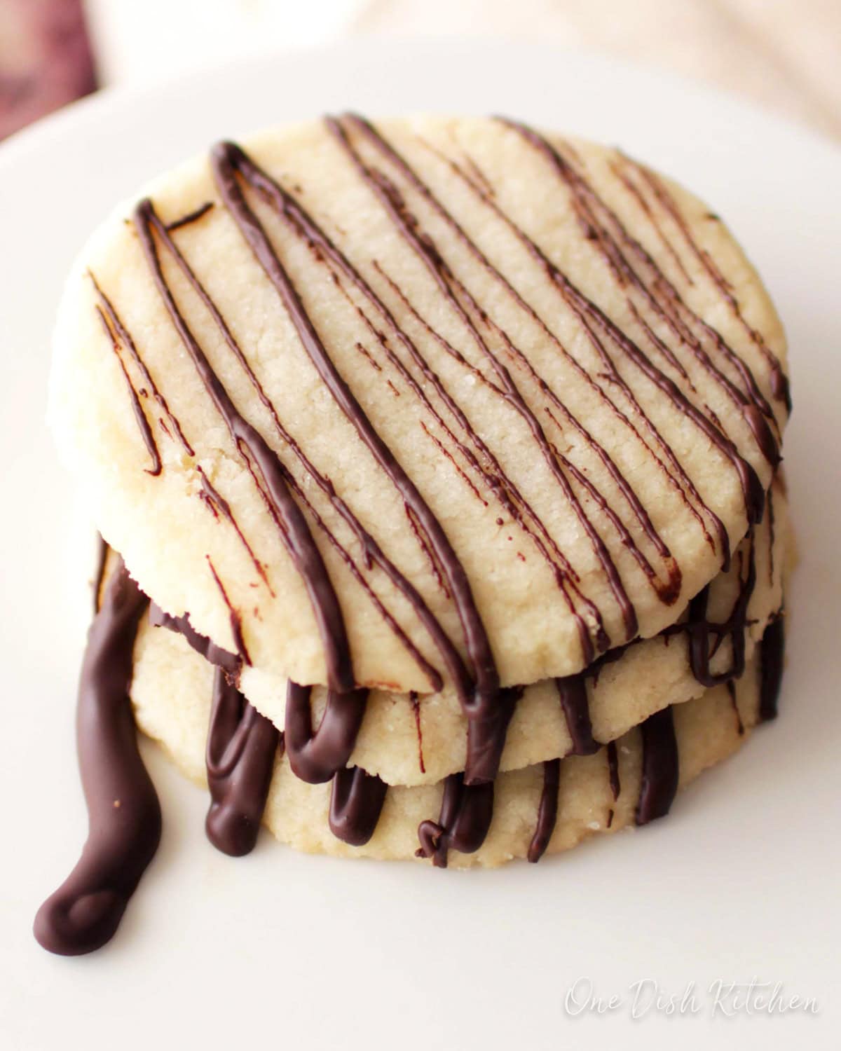 three shortbread cookies with a chocolate drizzle sitting on a cake stand.