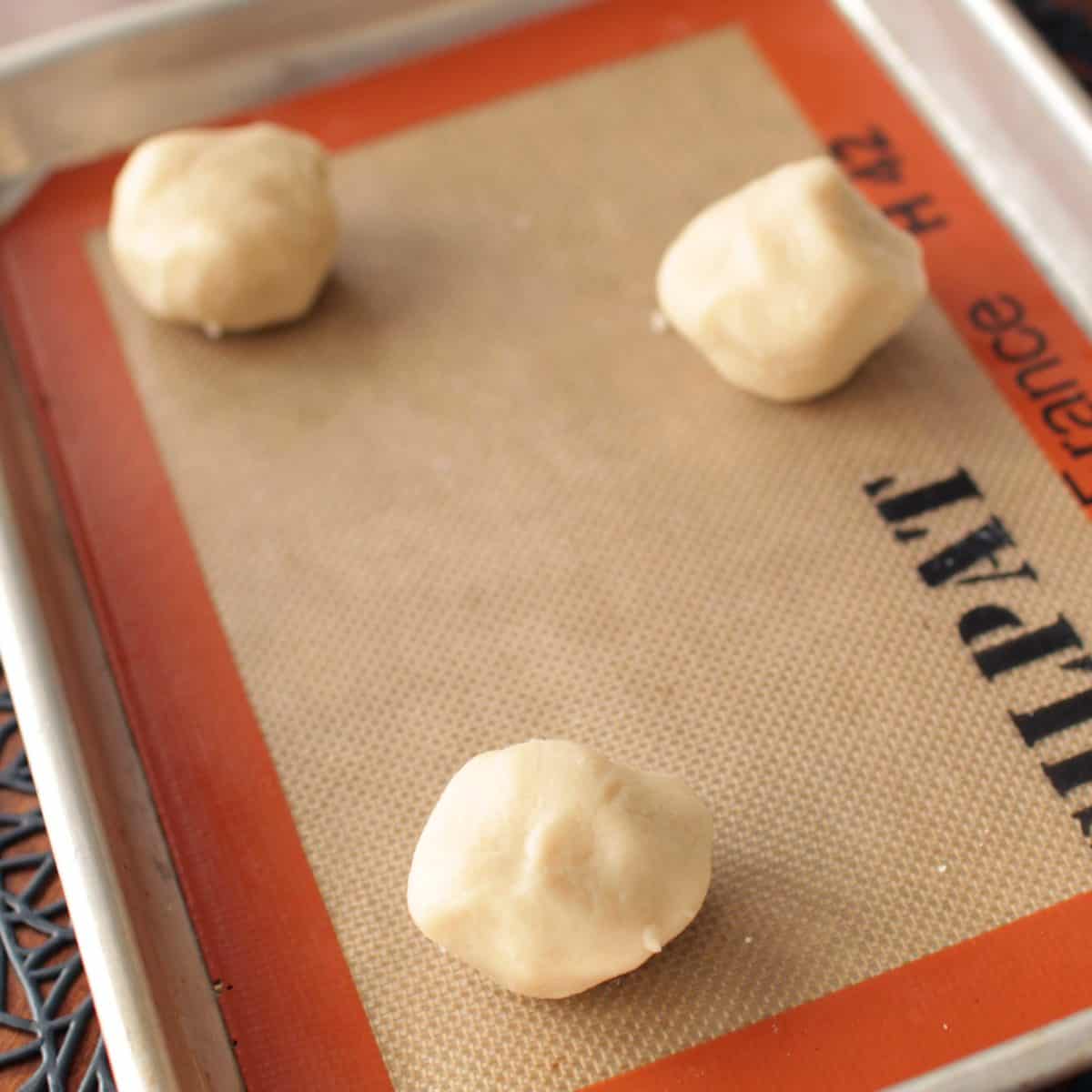 three balls of raw shortbread cookie dough on a baking sheet.