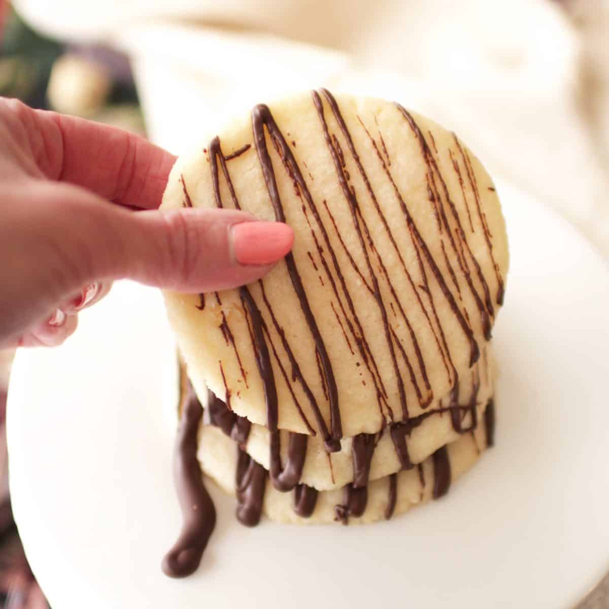 fingers holding up a shortbread cookie with a chocolate drizzle.