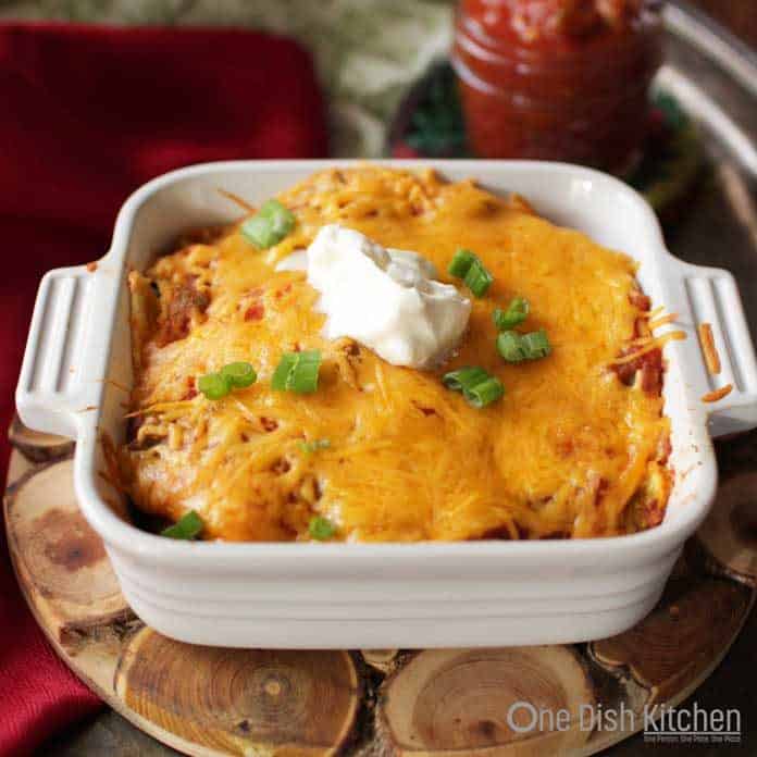 Vegetarian Enchiladas topped with sour cream in a small baking dish on a wooden trivet