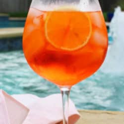 an aperol spritz next to a swimming pool.