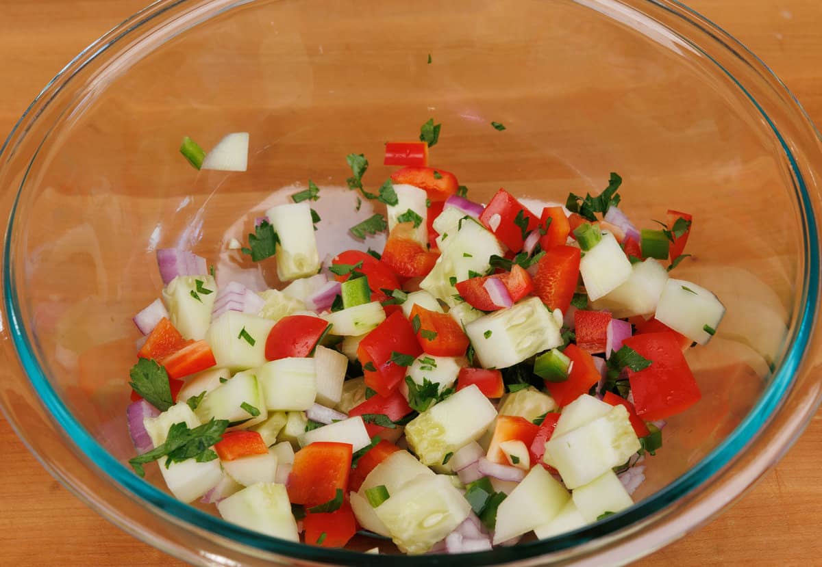 chopped cucumbers, onions, peppers, and cilantro in a mixing bowl