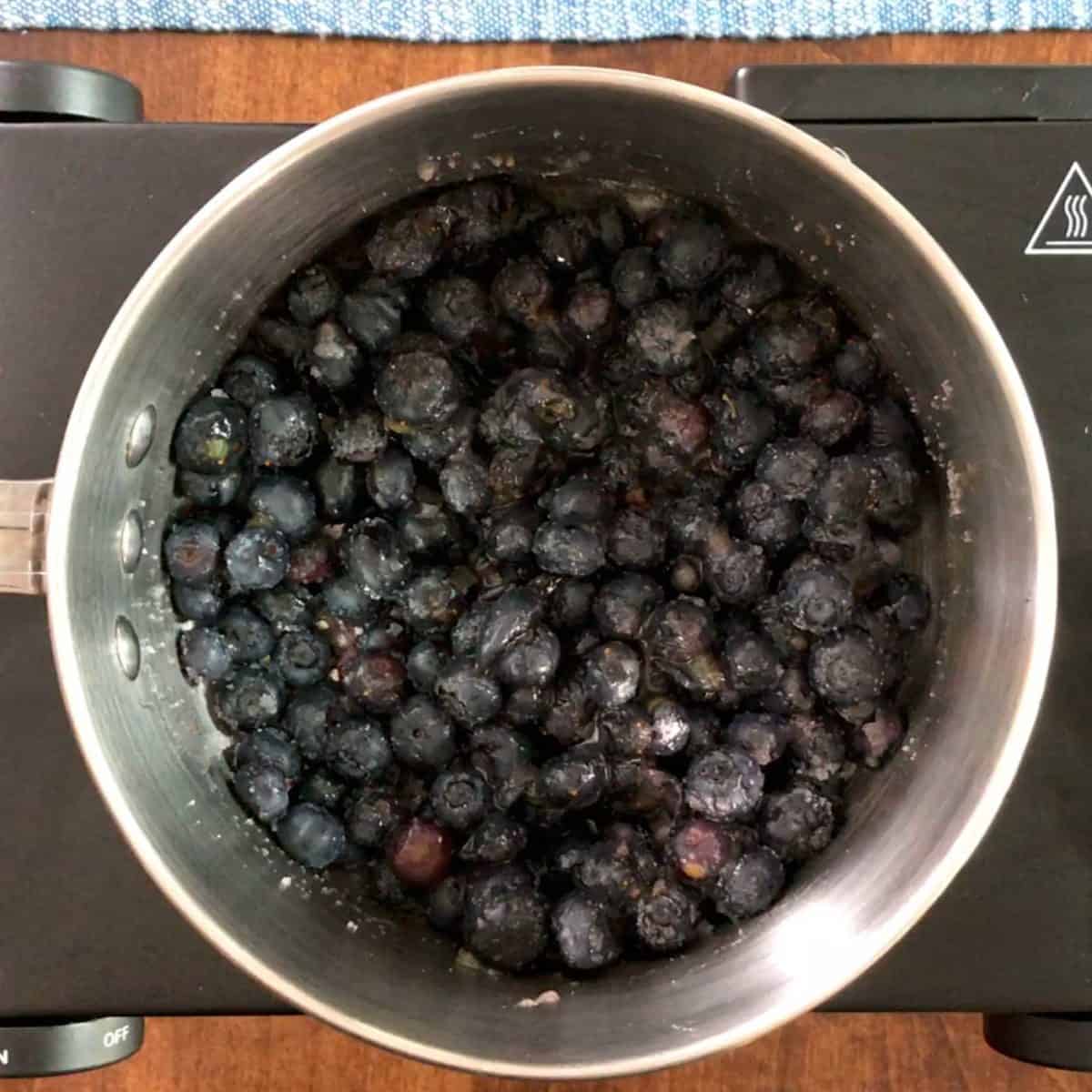 a pot filled with blueberries and sugar on the stove.