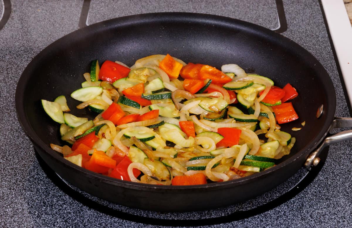 onions, peppers, and zucchini in a small skillet on the stove.