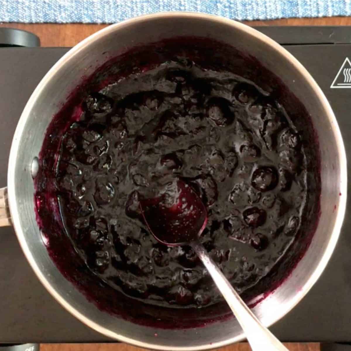 softened berries in a pot with a spoon on the side showing how to make homemade jam.