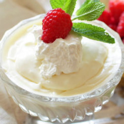a small bowl of vanilla pudding with a raspberry and a mint sprig on top