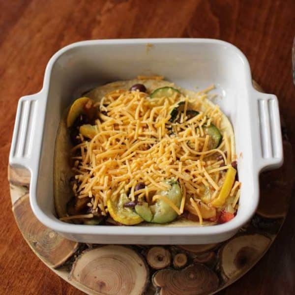 white baking dish with roasted vegetables covered with shredded yellow cheese