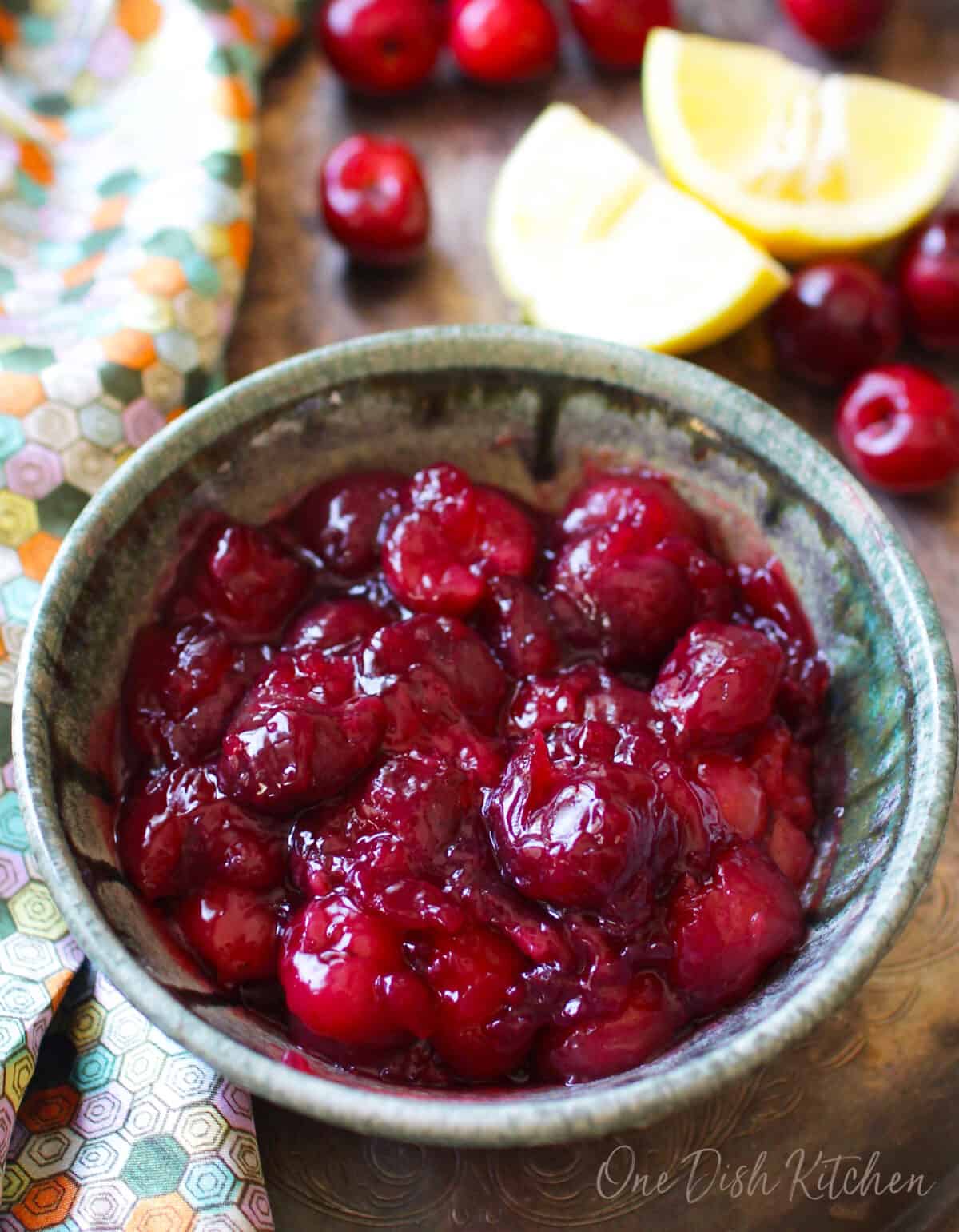 cherry pie filling in a blue bowl surrounded by fresh cherries.