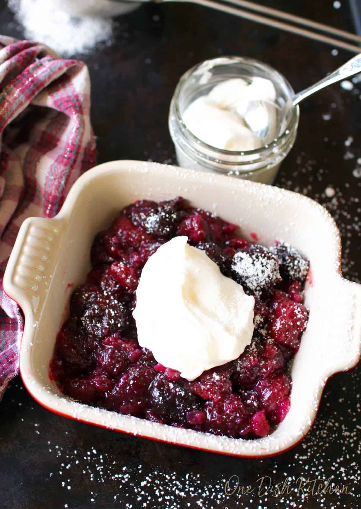 a small cherry pie next to a jar of whipped cream.