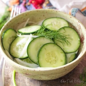 Single serving cucumber salad made with thinly sliced cucumbers, onion, fresh dill, and a light vinegar dressing in a small bowl.