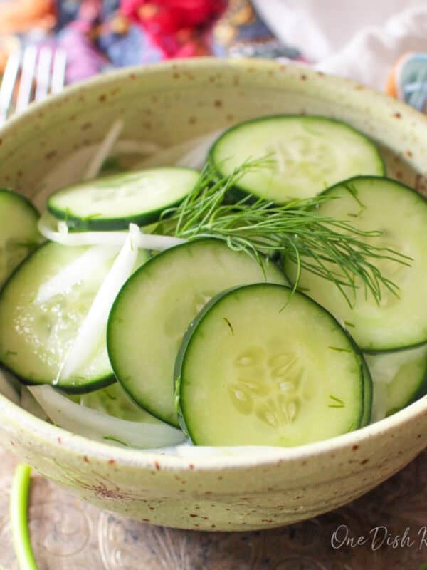 Single serving cucumber salad made with thinly sliced cucumbers, onion, fresh dill, and a light vinegar dressing in a small bowl.