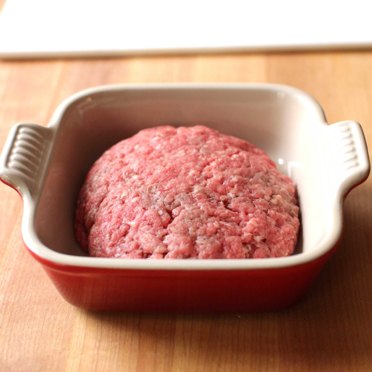 a juicy lucy burger in a small square baking dish on a wooden counter