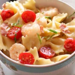 Shrimp and pasta in a bowl with tomatoes on top.