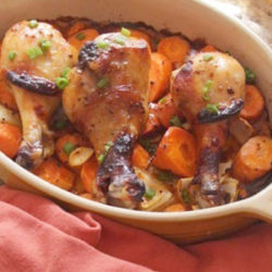 three chicken drumsticks on a bed of vegetables in a small baking dish next to an orange napkin