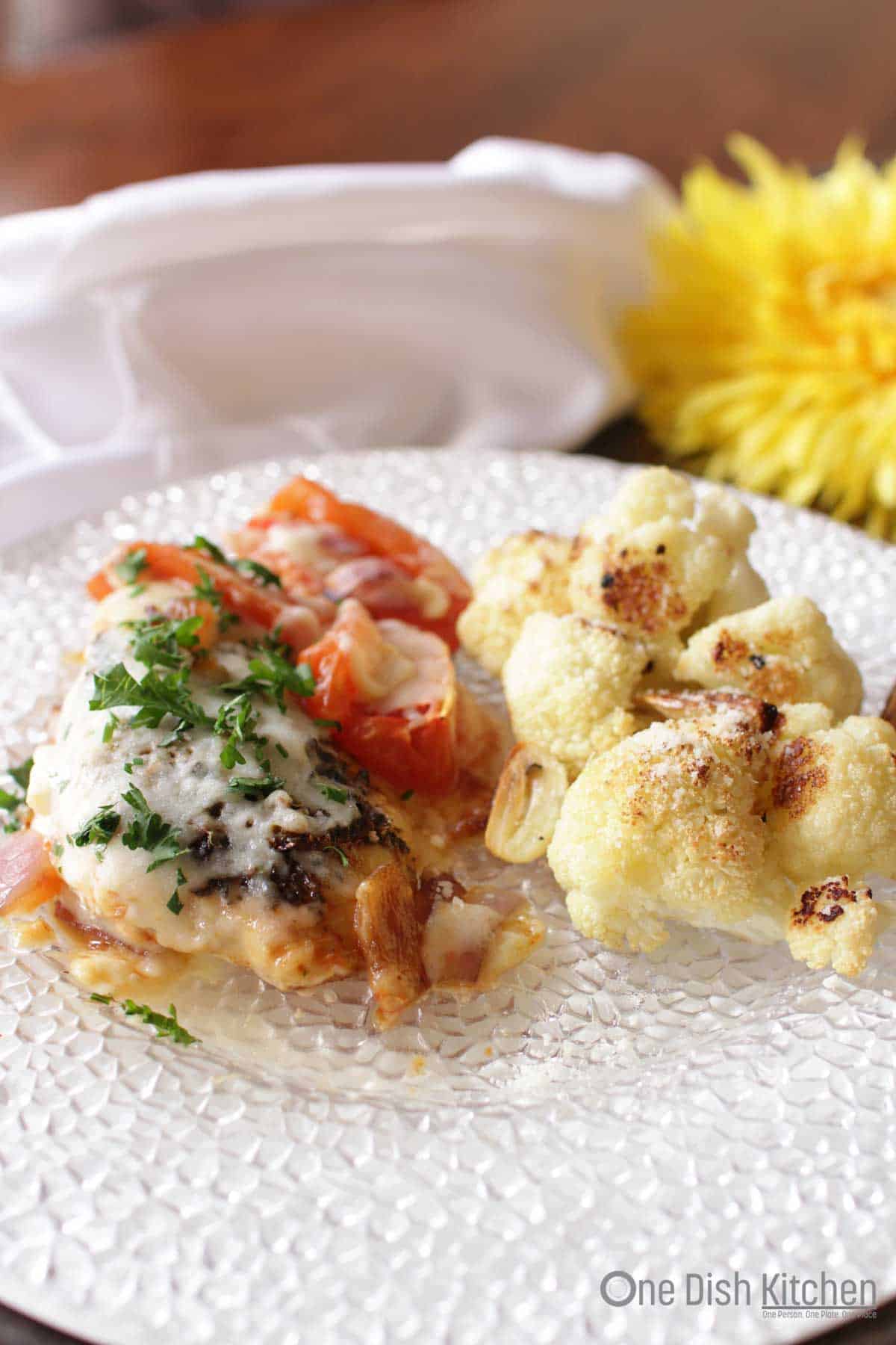 A plate of chicken caprese with a side of roasted cauliflower.