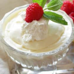 vanilla pudding in a clear glass with a raspberry and mint on top.