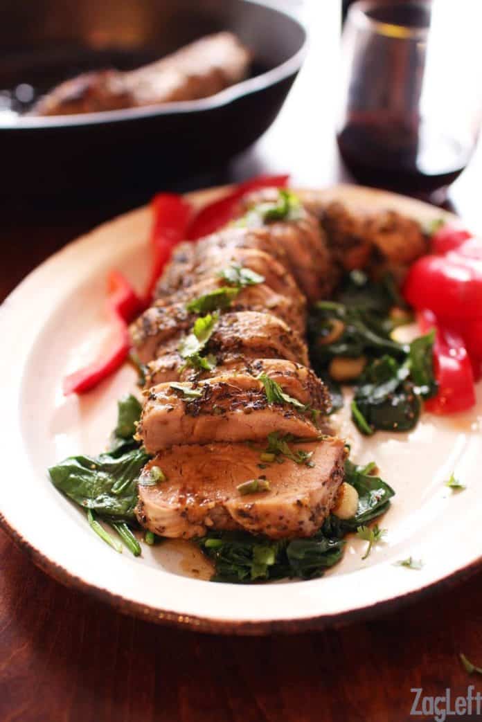 Sliced pork tenderloin on a white plate with spinach and sliced red peppers on a plate