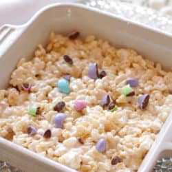 a large rice krispie treat in a square dish topped with pastel colored M & M's.