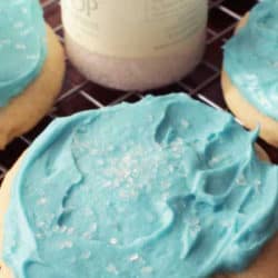 a sugar cookie with blue frosting and white sprinkles next to a glass of milk.