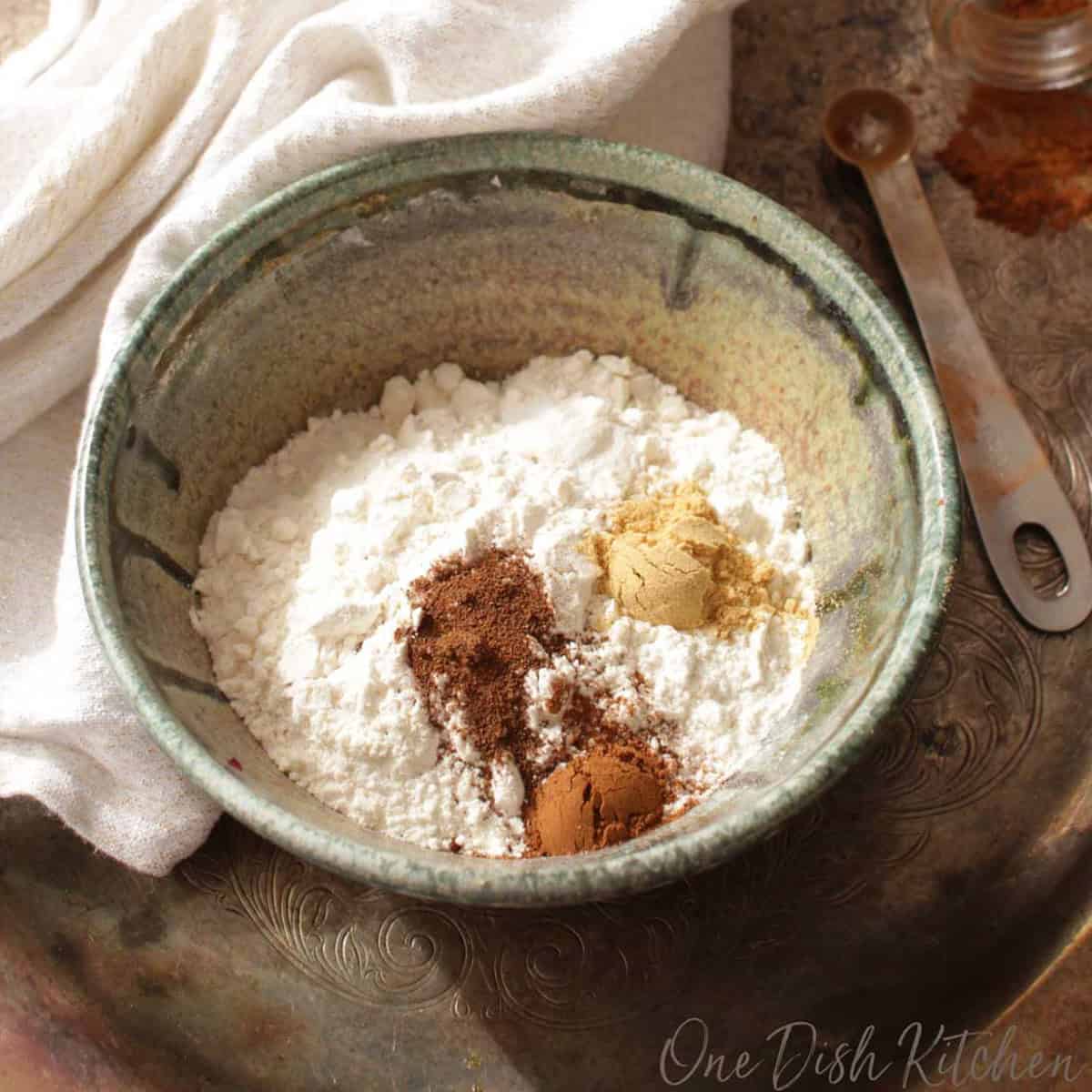 A bowl of spices for making ginger cookies on a metal tray with a white cloth napkin.