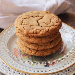 Four soft ginger cookies on a plate next to a white napkin