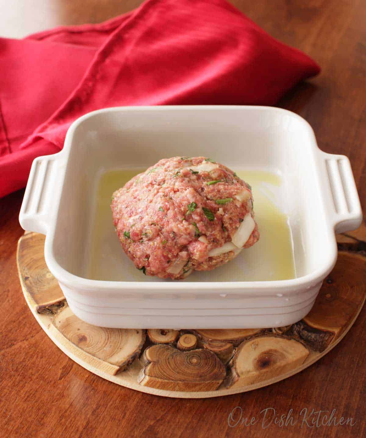 A meatball in a small baking dish on a wooden trivet.