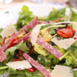 a salad with roasted vegetables and salami on a plate.