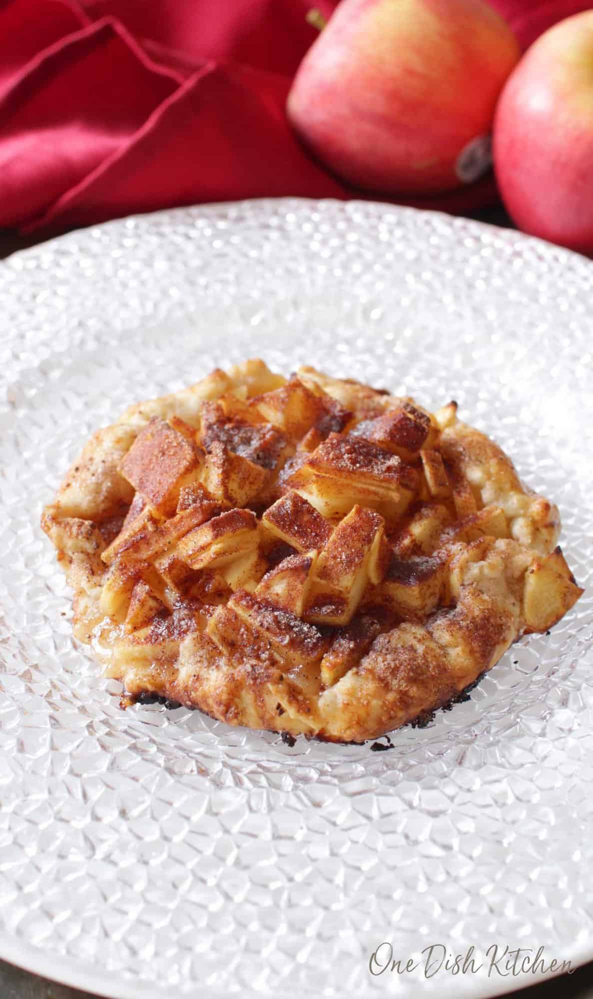 An apple galette topped with cinnamon and sugar plated with apples and a red cloth napkin in the background.