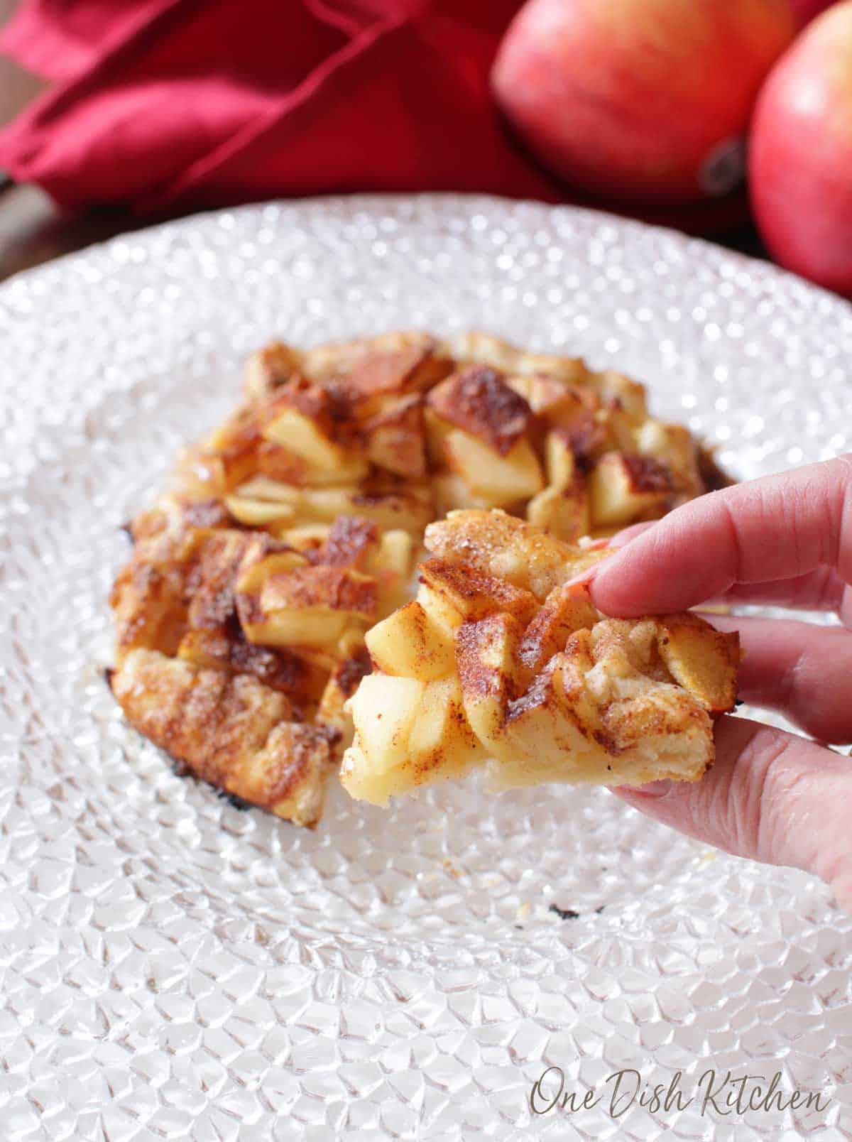 A closeup of fingers holding a piece of an apple galette.
