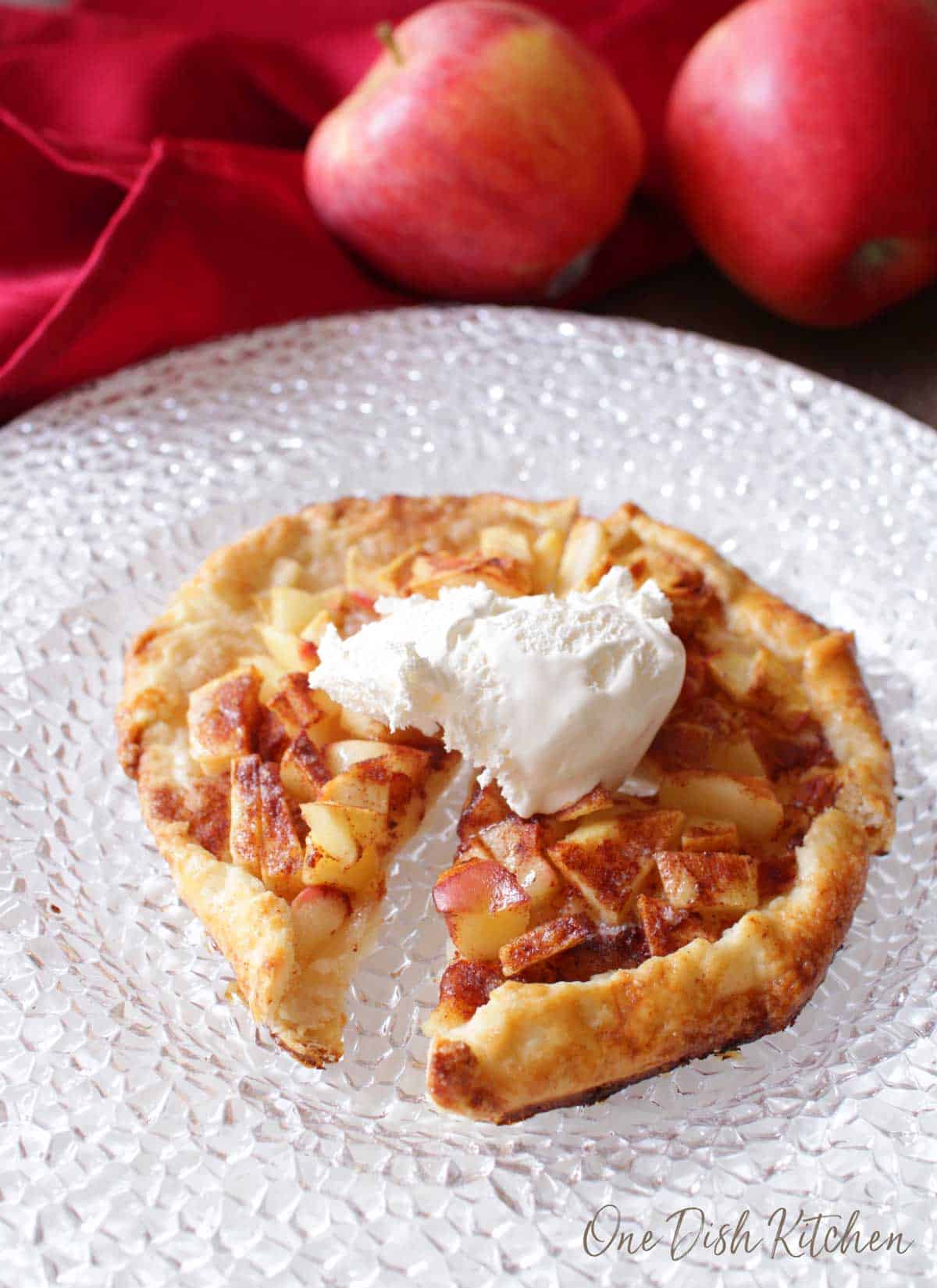 An apple galette topped with whipped cream cut into four slices.