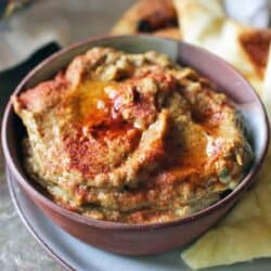 a bowl filled with roasted eggplant baba ganoush with pita chips on the side.