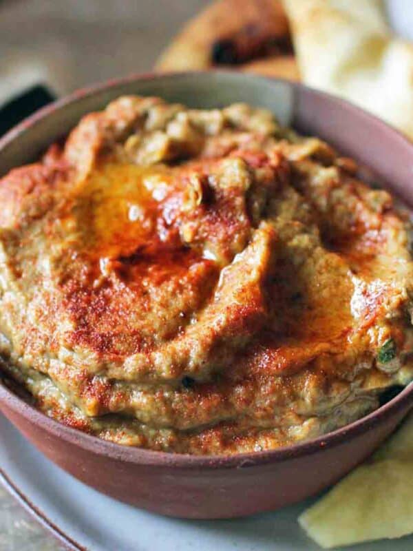 a bowl filled with roasted eggplant baba ganoush with pita chips on the side.