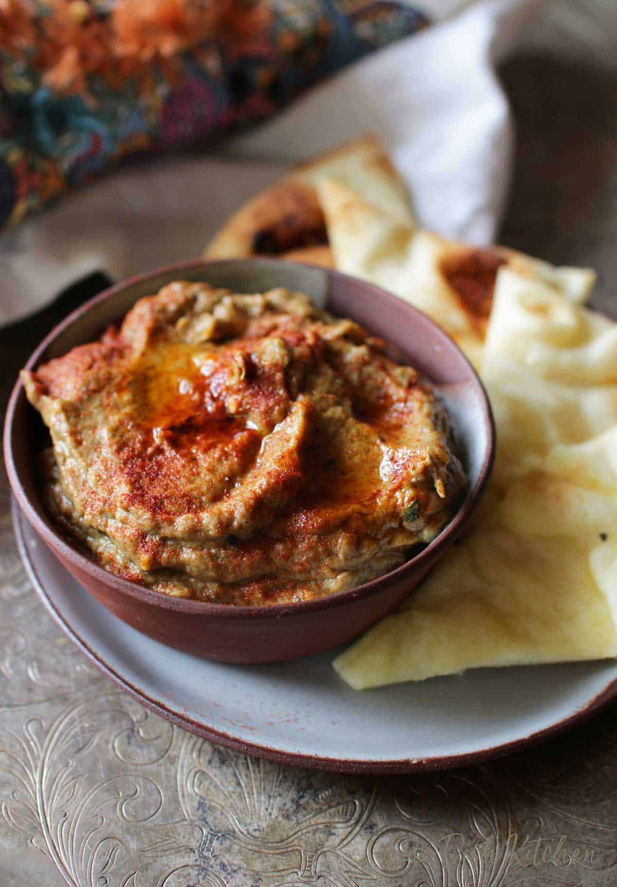 A bowl of baba ganoush plated with slices of pita bread
