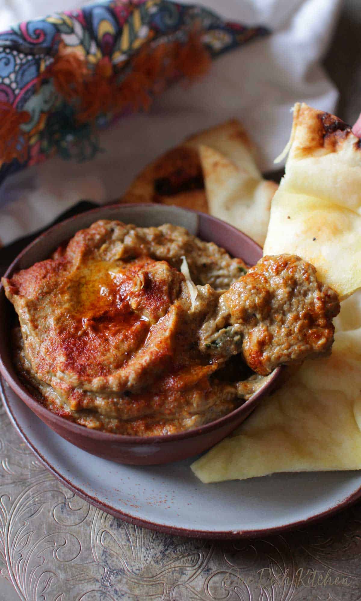 A slice of pita bread being dipped in a bowl of baba ganoush