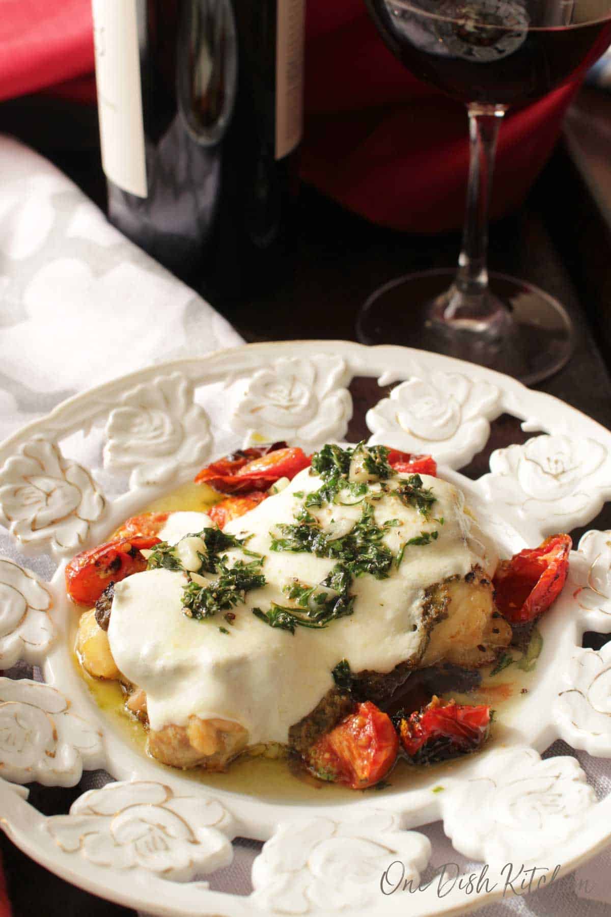 Chicken margherita on a plate with roasted cherry tomatoes next to a glass of red wine