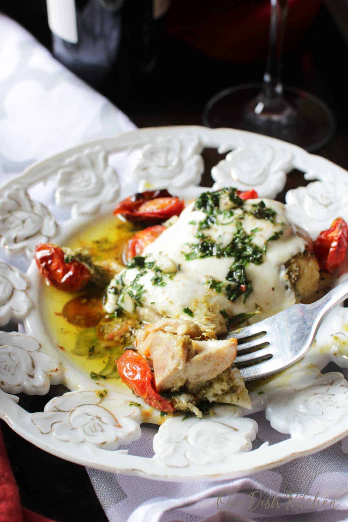 A forkful of chicken margherita from a plate with roasted cherry tomatoes. 