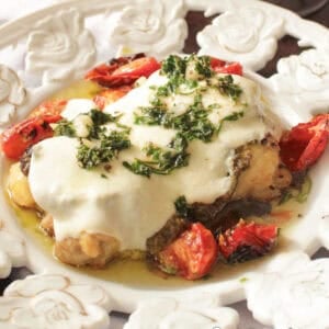 Chicken margherita on a plate with roasted cherry tomatoes next to a glass of red wine.